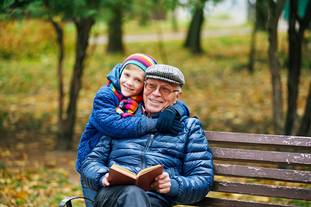 grandfather with his grandson reading a book while walking in the autumn Parkの写真素材