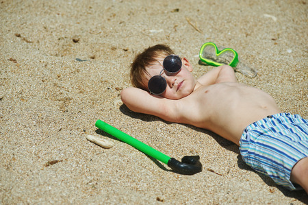 happy boy lying on the beach in glasses from the sunの写真素材