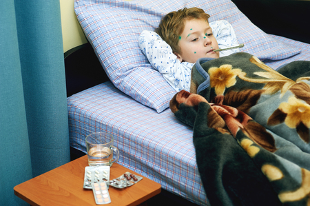 Sick child boy lying in bed with chicken poxの写真素材