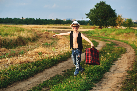 stylishly dressed boy in field with suitcaseの写真素材
