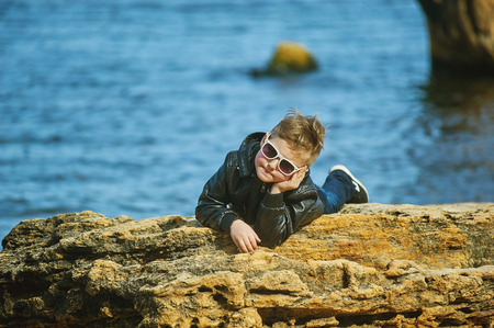 the boy in the glasses on the sea . A child posing in the spring lying on the stone on sea backgroundの写真素材