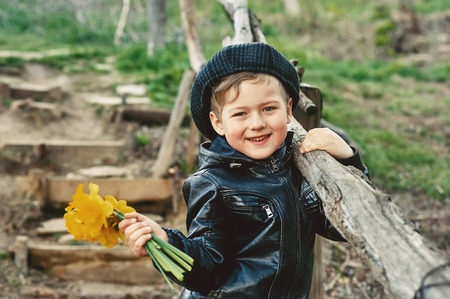 Stylish retro portrait of a boy in the countryside . Boy holding a bouquet of daffodilsの写真素材