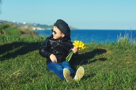 portrait of a boy on the beach . Boy holding a bouquet of daffodilsの写真素材