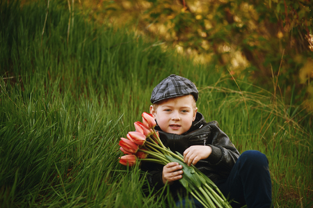 The boy on the lawn in spring with a bouquet of flowers . Spring gift .