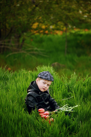 The boy on the lawn in spring with a bouquet of flowers . Spring gift .