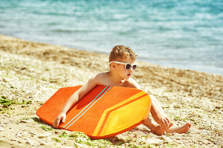 happy boy on the beach with a surfboard . The concept of summer vacationの写真素材
