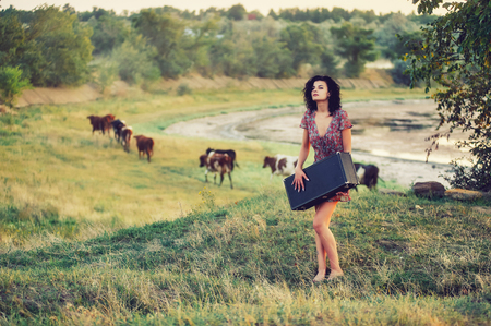 Beautiful young model girl in a summer dress in a field on a dirt road . The concept of rustic retro style clothingの写真素材