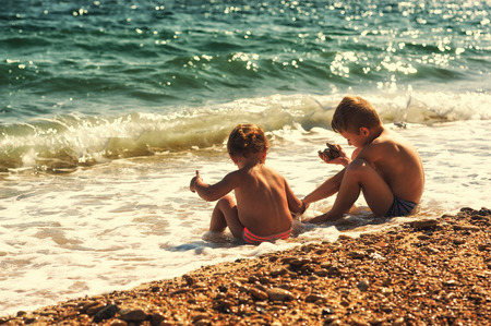 brother and sister playing in the sea in backlight
