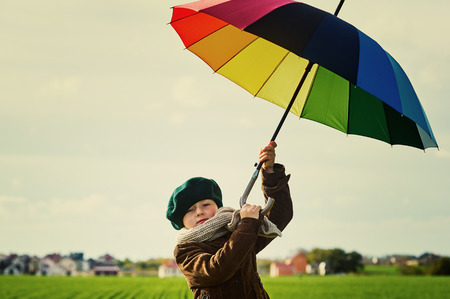 The child, standing under a colored umbrella on the green meadow .Retro style