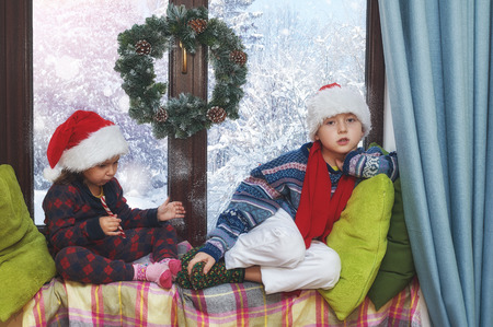 children sit by the window in the winter . Children waiting for Christmas .Merry Christmasの写真素材