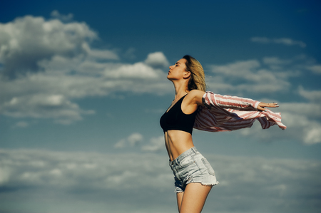 Happy young girl standing with outstretched arms against the sky , a young woman breathing fresh air.の写真素材