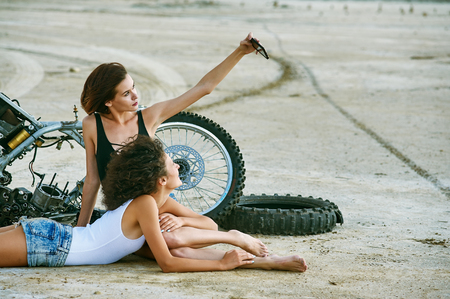 Two young women have fun playing on a disassembled motorcycle . Funny sexy girlsの写真素材