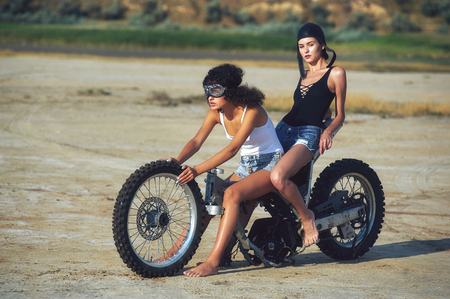 Two young women have fun playing on a disassembled motorcycle . Funny sexy girlsの写真素材