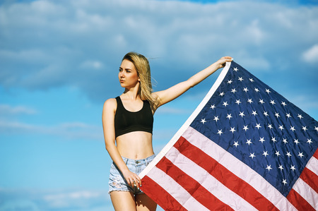 A young woman holding a us flag .The patriot girl with flag on sky backgroundの写真素材