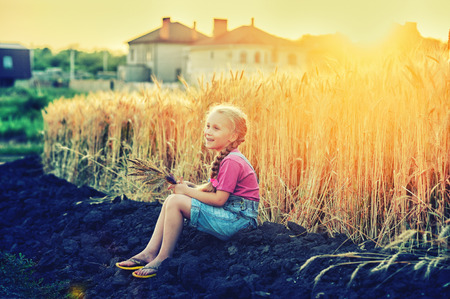 Cheerful girl on a walk at the field with wheat at sunsetの写真素材