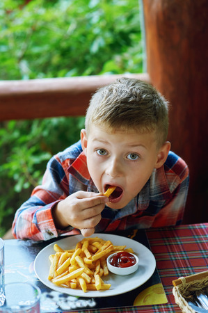 Boy eating French fries in a street cafeの写真素材