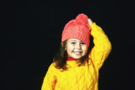 Close-up portrait of a little cheerful girl on a dark background . The child is dressed in a bright yellow jacket and hatの写真素材