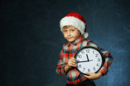 Portrait of a boy with a clock and a Santa hat on a dark background . Merry Christmasの写真素材