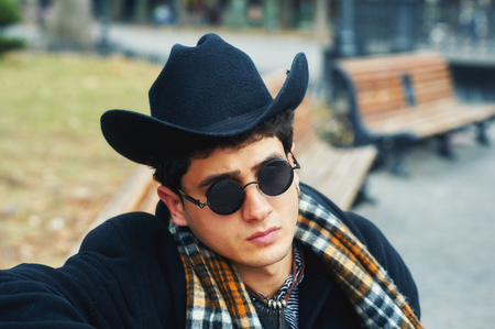 portrait of a stylish man on the street . man in black coat, plaid scarf and hat