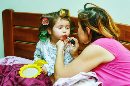Portrait of a little girl mom in curlers lying in bed. Morning little fashionistaの写真素材