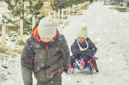 Winter fun in the fresh air . A little girl on a sled.Brother rubs sister sledgeの写真素材
