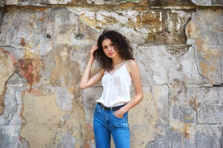 Young woman in jeans and white blouse at the old textured wallの写真素材