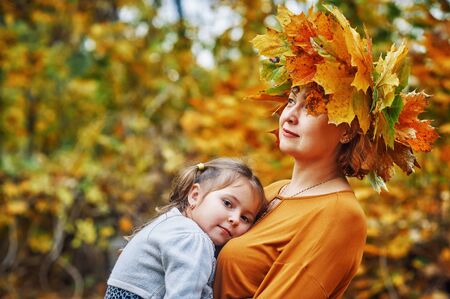 Portrait of a little girl and mother in the autumn Park, a girl with a wreath of maple leaves .の写真素材