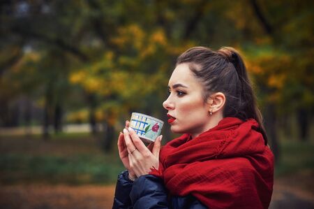 Portrait of a young happy woman with a Cup in the autumn Park