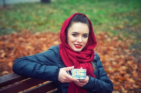Portrait of a young happy woman with a Cup in the autumn Parkの写真素材