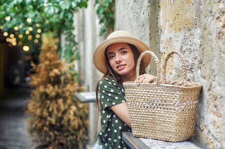 Beautiful young woman in fashionable straw hat on city street .の写真素材