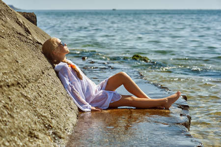 A little girl is resting at a seaside resort. A happy child in a white shirt takes a sun bath on the seaの写真素材
