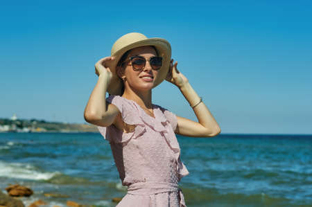 Portrait of a young woman in sunglasses and a straw hat on the sea coastの写真素材