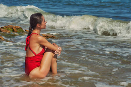 A young slender woman in a red swimsuit is resting on the sea coastの写真素材