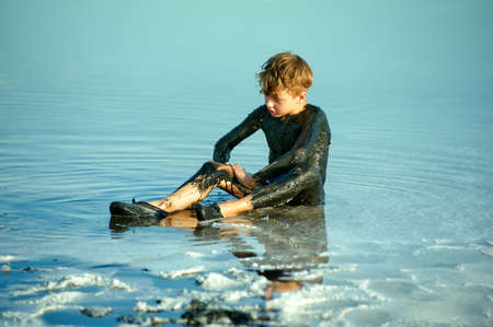 Happy little boy takes mud baths on the shore of the dead seaの写真素材