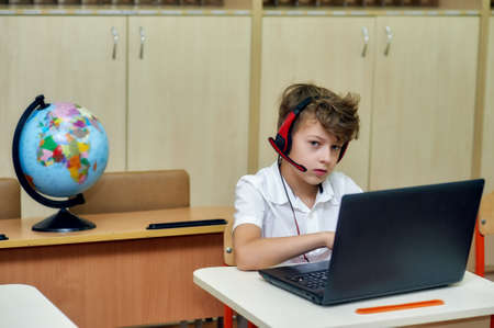 Portrait of an elementary school student in the classroom with a laptop and a voice headset in the classroom.の写真素材
