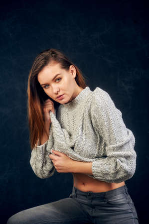 Portrait of a young beautiful girl in a warm knitted sweater on a dark backgroundの写真素材
