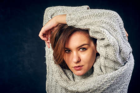 Portrait of a young beautiful girl in a warm knitted sweater on a dark backgroundの写真素材