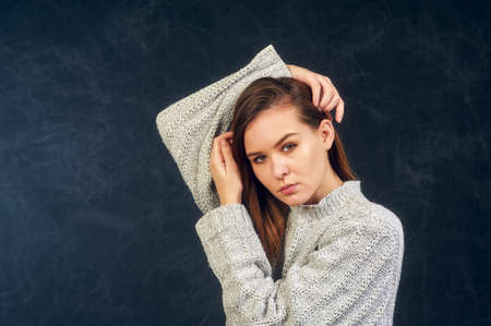 Portrait of a young beautiful girl in a warm knitted sweater on a dark backgroundの写真素材