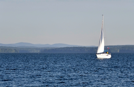 lonely sailing yacht on a calm morning lake, South Ural, Uvildy, in the distance are seen the Ural mountainsの写真素材
