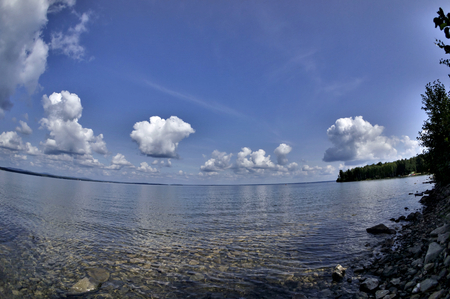 cumulonimbus white clouds above the clear water of the lake, you can see the rocky bottomの写真素材