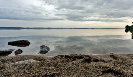 early morning on a calm lake in cloudy weather, water reflects clouds, no wind, silenceの写真素材