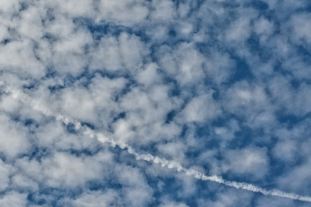 texture of the blue sky with thin white ragged clouds crossed out by a curve stroke from a jetの写真素材