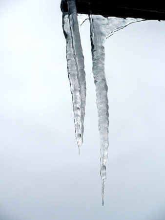 long icicles hanging from the roof against the overcast gray skyの写真素材