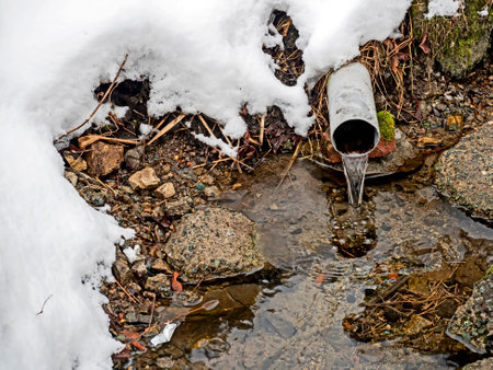 Clear, clean water from a spring source flows from a pipe into a rocky bedの写真素材