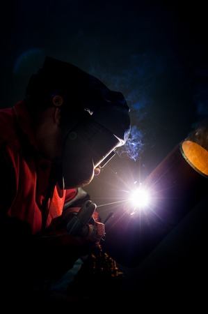 Welder working in the red uniform and a mask, he welds pipe bright sparks fly