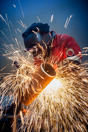 Welder working in the red uniform and a mask, he welds pipe bright sparks flyの写真素材