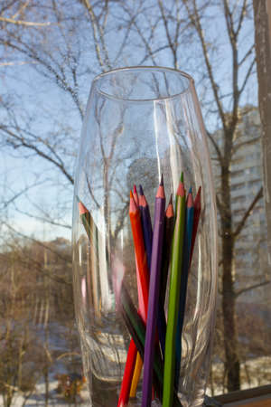 colored pencils in a glass beaker on the windowsillの写真素材