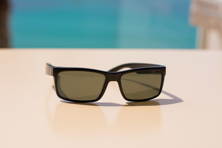 One pair of sunglasses on a table with a nice palm tree and the sea on the blurred background. The perfect summer photo.の写真素材