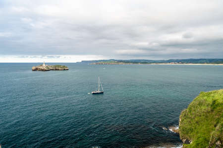 SANTANDER, SPAIN - JULY 9, 2021: View from the Magdalena Peninsula, Santander, Spain, with a small boat sailing and the Mouro Island in the background with its 19th century lighthouseのeditorial素材