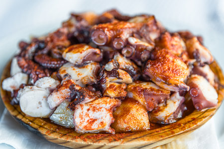 Galician-style octopus dish, served on its typical wooden plate; consists of cooked octopus slices, drizzled with olive oil, paprika and saltの写真素材